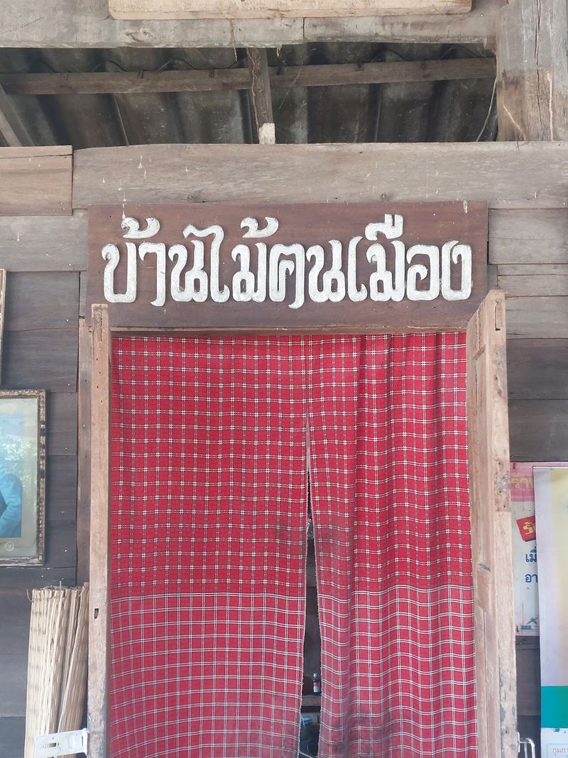 ป้ายไม้เขียนชื่อร้านบ้านไม้ฅนเมือง เหนือม่านผ้าลายตารางสีแดง
