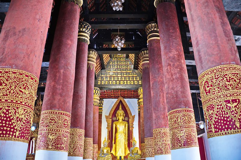 เสาสีแดงลายทองเรียงเป็นแถว ปลายทางเป็นพระพุทธรูปยืนสีทอง
